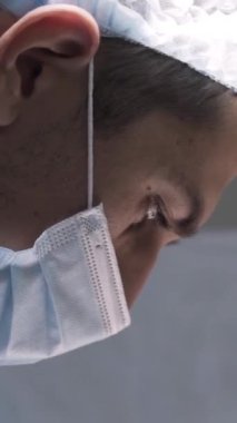 Ameliyat yapan genç cerrahın yakın çekimi. Başla. Maskeli yakışıklı adam anestezi altında karmaşık operasyonlar yapıyor. Güzel profesyonel cerrah.