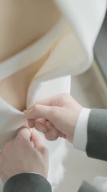 Koca, gelininin düğmelerini ilikliyor. Başla. Kocanın gelinlikleri bağlamasına yardım ettiği yakın çekim. Koca, karısına romantik bir şekilde bağlanır..