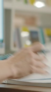 Kadın öğretmen, sınıftaki bir masada rafların kitaplarıyla ödevlerini kontrol ediyor. Stok görüntüleri. Kağıt bir defterin sayfalarını çeviren bir kalemle kadın ellerini kapat ve not al.