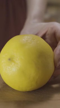 Evin mutfağındaki ahşap bir tahtanın üzerinde sarı limonu çelik bıçakla kesen kadın ellerine yakın çekim. Başla. Limonata hazırlama süreci