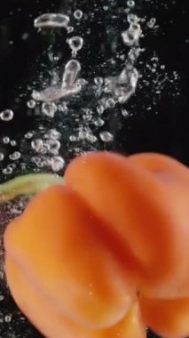 Hava kabarcıklarıyla suya düşen taze kırmızı tatlı biber. Başla. Lezzetli sebzelerin siyah arka plandaki su deposuna atılmasını yavaş çekimde kapat.