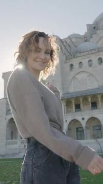 Tapınağın arka planında poz veren güzel bir kadın. Başla. Mutlu kadın güneşli bir günde caminin dışında dans eder. Güneş ışınlarının arka planında camiye yakın daireler çizen güzel bir kadın..