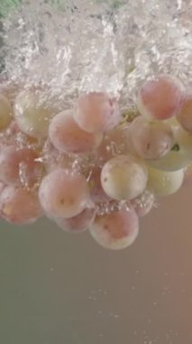 Üzüm dalı yeşil ve bej arka planda şeffaf suya düşüyor. Başla. Akvaryuma hava kabarcıkları, sağlıklı yiyecek konsepti ve diyet ile su sıçratan taze böğürtlenleri kapatın.