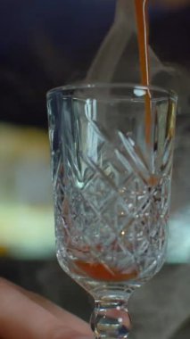 Bardaki barmenin bardağına içki dökerken yakın plan. Medya. Sıcak, sıcak, buharlı alkol tentürü.