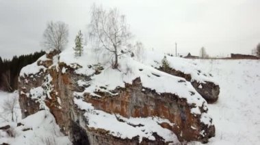 A serene winter scene with a rocky outcrop covered in soft snow and scattered trees dotting the landscape. Stock Clip