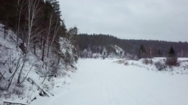 Huzurlu bir kış sahnesi, sakin bir ormanlık alanda yavaşça kıvrılan karlı bir nehri gösteriyor. Menkul Kıymetler