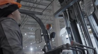 Kendini işine adamış ve yetenekli bir işçi yoğun ve yoğun bir depo ortamında ağır bir forklift kullanıyor. Kırp