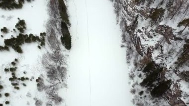 Ağaçların arasında dolanan dar dolambaçlı bir yolu olan engin, karlı bir araziyi güzel bir şekilde çeken bir hava görüntüsü. Menkul Kıymetler