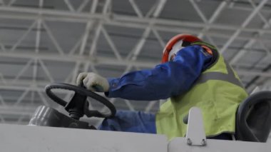 Kendini adamış bir depo işçisi, güvenlik donanımı takıyor, hassas ve dikkatli bir şekilde ağır makineler kullanıyor. Kırp