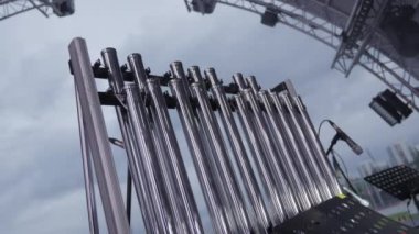 Bulutlu bir gökyüzünün altında gerçekleşen eşsiz bir müzikal performansta kullanılan metalik boruların yakın plan çekimi. Kırp