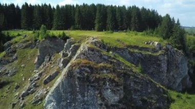 Havadan bakıldığında, canlı yeşillikler ve manzarada yüksek ağaçlarla çevrili engebeli bir kaya oluşumu görülüyor. Kırp