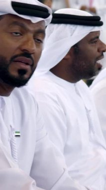 Dubai, BAE - Haziran 2024: Geleneksel kıyafetlerini giymiş Emirati erkekleri canlı bir kültürel etkinlikte aktif olarak diyalog içine giriyorlar. Medya