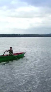 Yalnız bir kanocu, bulutlu bir gökyüzünün altındaki manzaranın tadını çıkararak sakin ve pürüzsüz bir gölde yavaşça kürek çekiyor. Menkul Kıymetler