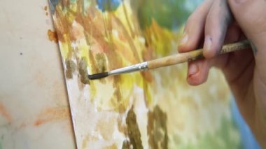 Becerikli bir sanatçı, tuval üzerinde fırçası olan canlı ve renkli bir manzara resminin detaylarını titizlikle anlatır. Eylem