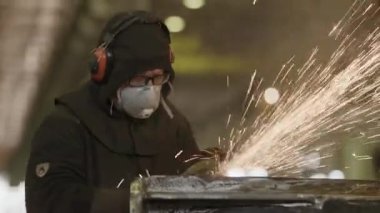 Etrafında kıvılcımlar uçuşurken atölye ortamında metal öğüten çalışkan ve odaklanmış bir sanayi işçisi. Menkul Kıymetler