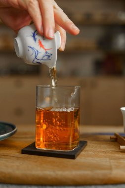 Nazik bir el, bir çaydanlıktan narin bir cam fincana hoş kokulu çay döker, dingin bir çay anını vurgular.