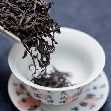 Güzel koyu siyah çay yaprakları dikkatli bir şekilde Çin çay fincanının içine dökülüyor.