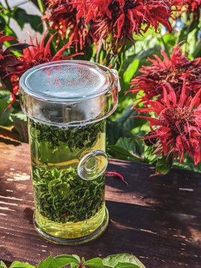 Canlı ve aromatik bir bitki çayı yemyeşil yapraklar ve renkli çiçekler arasında güzelce sergilenir.