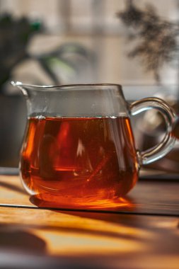 Zengin kehribar çaydanlığıyla dolup taşan güzel bir cam çaydanlık kırsal bir ahşap yüzeyde dinleniyor, çay severler için ideal.