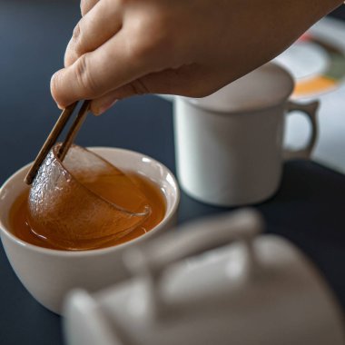 Balı bir fincan buharlı çaya bandırmak için yemek çubuklarını incelikle kullanan bir el huzurlu bir çay anı sergiliyor.