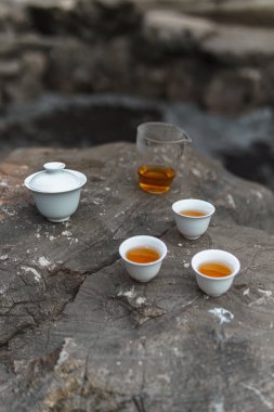 Sakin suların kıyısındaki kayalık bir yüzeyde demlik ve fincanlarla kurulmuş sakin bir çay sükuneti ve huzuru temsil eder.