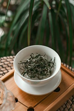 Yeşilliklerle çevrili bir kasede canlı yeşil çay yaprakları sergilenmesi rahatlatıcı bir titreşim yaratıyor.