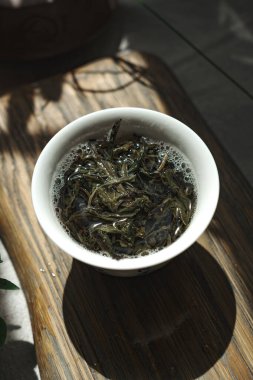 Güzel, sakin bir sahne, ahşap tepsiye konmuş taze demlenmiş yeşil çay bardağını gösteriyor.