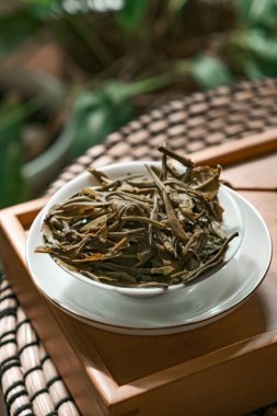 Kırsal ahşap tepside kurumuş yeşil çay yapraklarının huzurlu bir görüntüsü doğal güzelliklerini detaylarıyla gözler önüne seriyor.