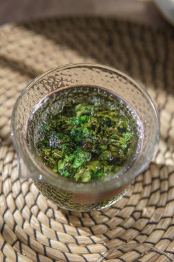 Canlı bir bardak bitkisel çay. Taze toplanmış yeşil otlar sergileniyor. Refah ve rahatlama için ideal.