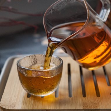 Narin, cam bir çaydanlık, kristal berrak bir fincana nazikçe çay döküyor, hepsi de ahşap bir tepside zarif bir şekilde sergileniyor.