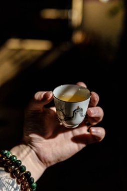 Huzurlu bir atmosferde, sıcak ışıkla aydınlatılmış narin bir çay fincanını tutan bir elle sakin bir an.