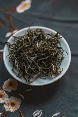 Seramik bir tabakta kurumuş yeşil çay yapraklarının estetik görüntüsü. Çiçek kumaşının arka planında.