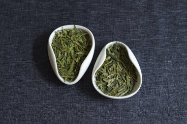 Koyu bir yüzeyde, canlı yeşil çayla dolu iki kase vardır. Renkleri ve dokuları güzelce sergilenir.