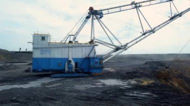Geniş ve dramatik bulutlu bir gökyüzünün altında büyük bir mavi kazıcı aktif olarak bir maden sahası üzerinde çalışıyor. Menkul Kıymetler