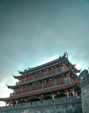 Huysuz bir gökyüzünün altında parlak fenerlerle süslenmiş antik bir Çin mimari mucizesinin çarpıcı bir görüntüsü.