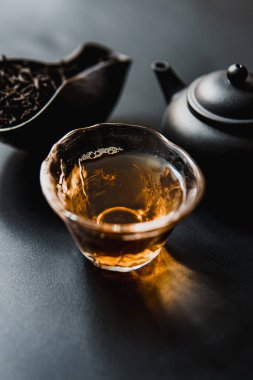 Cam bir bardak, zarif bir çaydanlık ve aromatik aromalı çay yaprakları sergilenen güzel bir çay sahnesi.