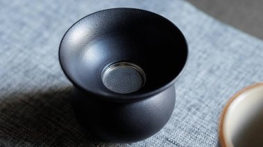 Göz alıcı derecede minimalist siyah bir fincan, karmaşık desenli keten kumaş arka planına karşı güzelce düzenlenmiştir.