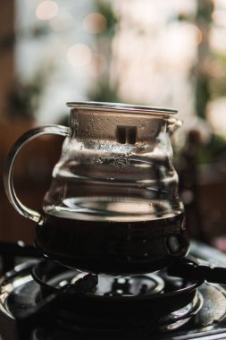 Sade, siyah bir sobanın üzerinde cam bir kahve demliği sergileniyor. Sıcak, davetkar bir ortamda taze demlenmiş kahve.