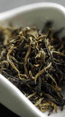Kurutulmuş çay yapraklarının yakın çekimi eşsiz dokularını ve renk çeşitlerini bir tabakta zarif bir şekilde sunar.