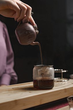 Bir el, bir çaydanlıktan cam bir kavanoza sıcak çay dolduruyor. Huzurlu bir demlenme anını güzel bir şekilde gösteriyor.