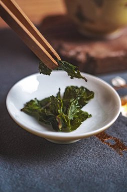 Taze, canlı yeşil çay yapraklarının detaylı ve yakın görüntüsü çubuklarla dikkatlice toplanıyor.