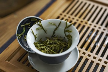 Tahta bir tepside çay fincanındaki taze yeşil çay yapraklarının yakın çekimi, sahneleri sükunet vurguluyor.