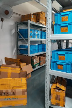 Düzenli bir depolama alanı, verimlilik için karton kutuların yanında düzenli olarak düzenlenmiş mavi kutularla karakterize edilir.