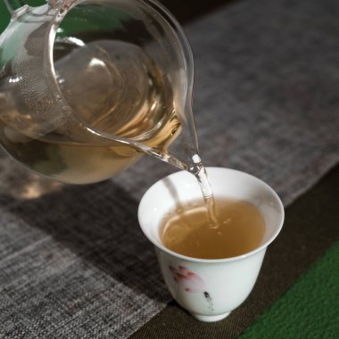 Çay hazırlama sanatının sergilendiği narin bir fincanın içine dökülen bitkisel çayın huzurlu bir görüntüsü..