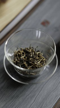 Güzel ahşap bir yüzey üzerinde şeffaf cam bir kâse içinde açık yeşil çay sergilenen detaylı bir yakın çekim görüntüsü.