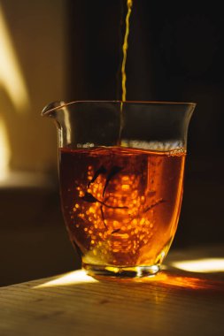 Güzel yansımaları ve zengin kehribar tonlarını sergileyen temiz bir bardağa nazikçe dökülen çayın yakın plan görüntüsü.