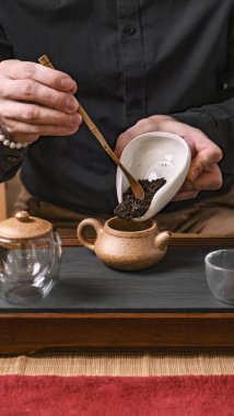 Karmaşık bir çay seremonisinin yakın plan görüntüsü, çay yapraklarının dikkatlice çaydanlığa dökülmesi.