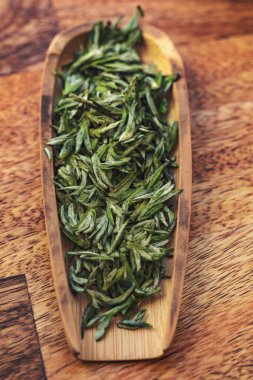 Kurumuş yeşil çay yapraklarının estetik görüntüsü. Büyüleyici bir masanın üstündeki ahşap bir tabakta düzenlenmiş.