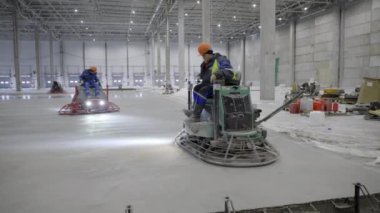 İşçiler, büyük bir inşaat alanında troweling makineleriyle yeni dökülmüş beton zemini düzeltiyorlar. Kırp