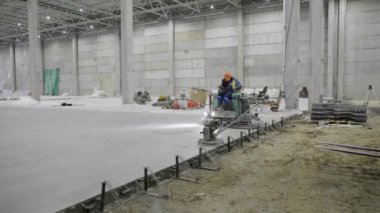 Bir işçi, büyük bir sanayi tesisine pürüzsüz bir beton zemin kurmak için ağır makineler kullanıyor. Kırp